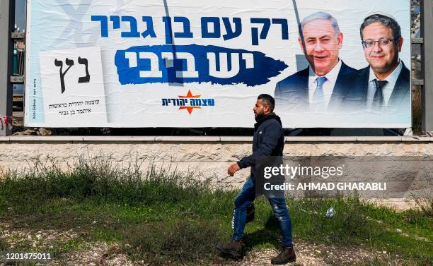 Man walks past an Israeli Otzma Yehudit party electoral campaign billboard for the upcoming legislative elections showing the faces of Israeli Prime...