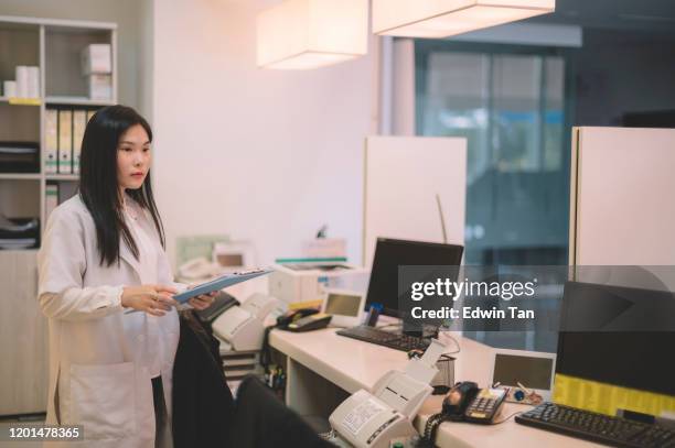 een aziatische chinese vrouwelijke arts die zich bij de het tegenbestand van de ziekenhuisontvangst bevindt die een medische grafiek houdt - faxmachine stockfoto's en -beelden