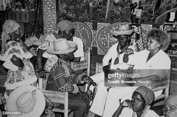 View of American dancer, choreographer, and activist Katherine Dunham as she sits with unidentified, traditional Haitian Voodoo dancers, Carrefours,...