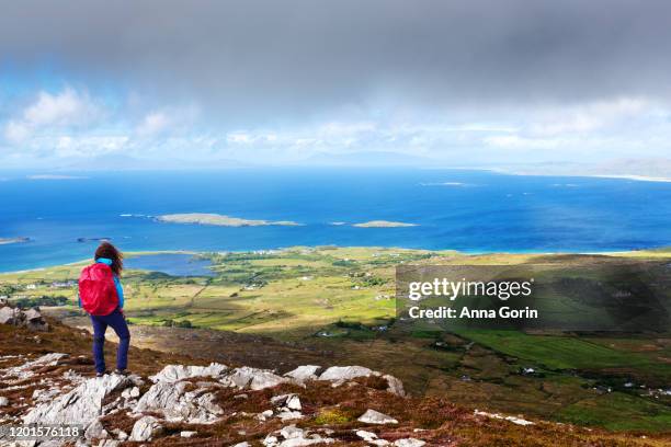 back view of woman wearing red backpack standing at summit of tully mountain, spring evening in western ireland, county galway - galway stock pictures, royalty-free photos & images