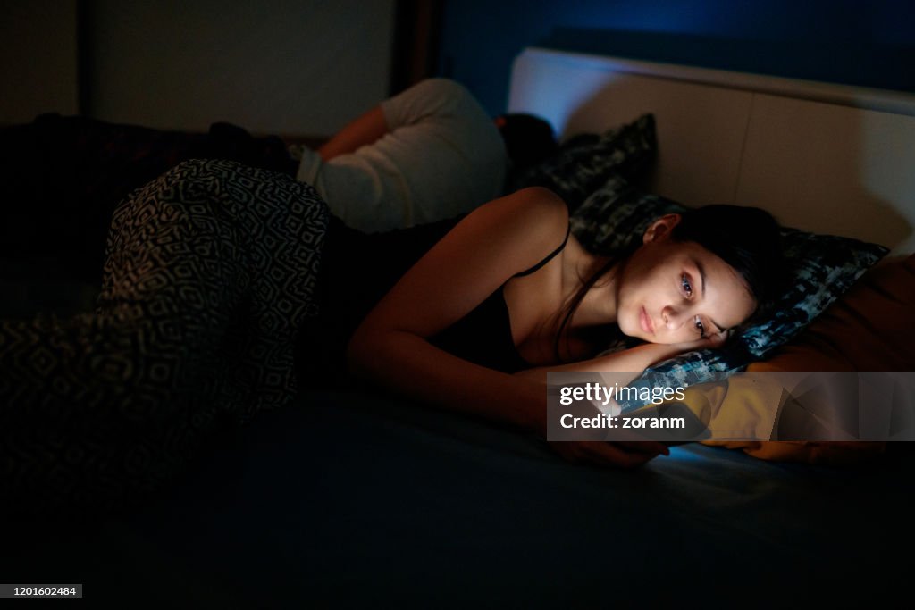 She is checking her smartphone at bedtime