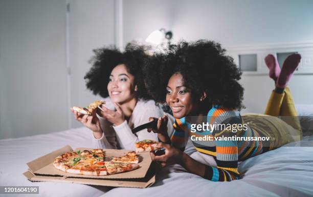 girlfriends eating pizza in bed and watching tv - part of a series stock pictures, royalty-free photos & images
