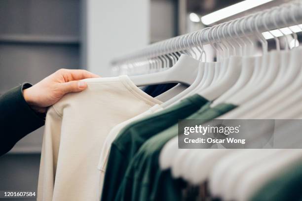 cropped hand of man holding shirt in shop - customer intelligence stock pictures, royalty-free photos & images