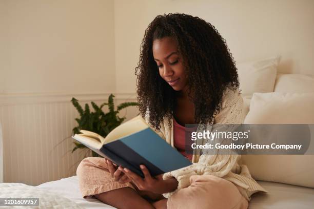 young woman sitting on her bed reading a novel - reading stock pictures, royalty-free photos & images