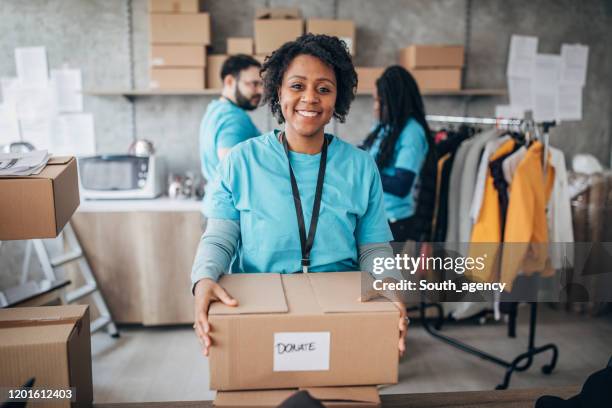 black woman volunteer packing donation boxes in charity food bank - giving tuesday stock pictures, royalty-free photos & images