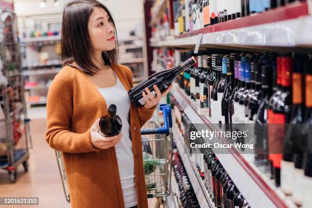 young asian woman choosing wine in grocery store - buying alcohol stock pictures, royalty-free photos & images