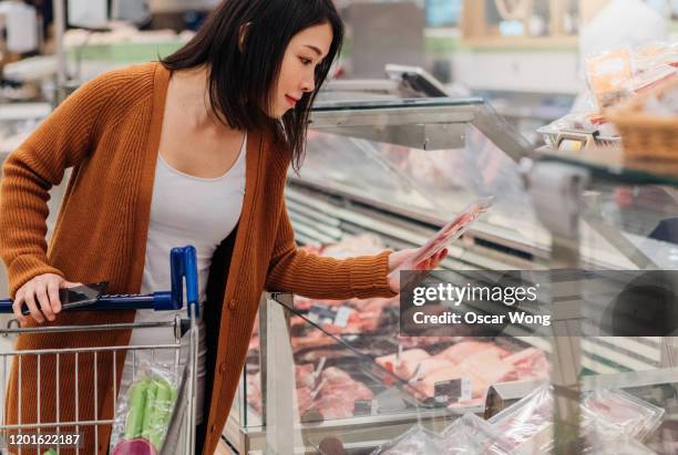 young asian woman choosing meat in grocery store - ham salami stock pictures, royalty-free photos & images