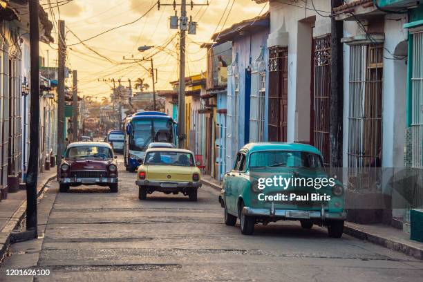 sunset light shining on street with old cars in trinidad, cuba - cuba car stock pictures, royalty-free photos & images