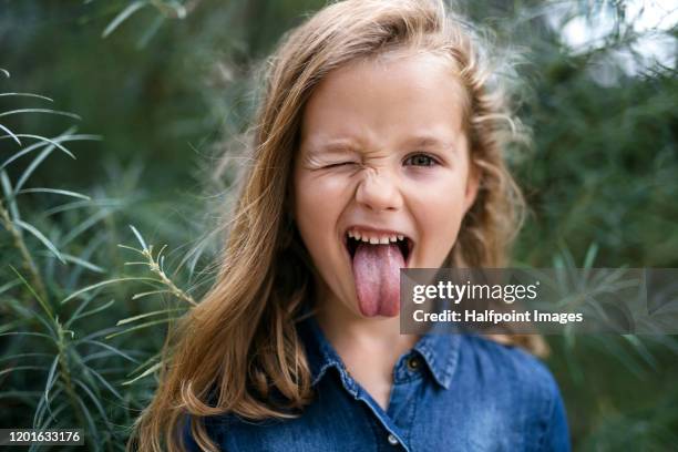 front view portrait of small girl standing outdoors, sticking out tongue. - poner caras fotografías e imágenes de stock