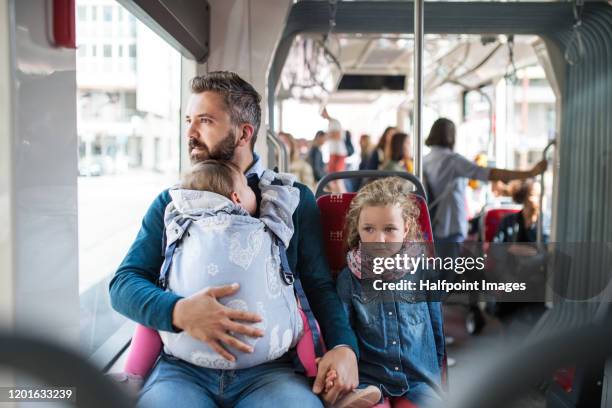 father with daughter and toddler in carrier sitting on bus in city, travelling. - kids sitting together in bus stock-fotos und bilder