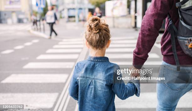 rear view of small girl with father walking outdoors in city, crossing the road. - attraversare foto e immagini stock