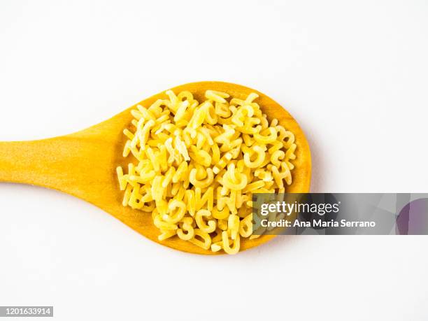 directly above shot of raw letters soup in a wooden spoon against white background. - alphabet soup stock pictures, royalty-free photos & images
