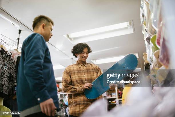 junger mann bei der wahl eines skateboards - sport shop stock-fotos und bilder