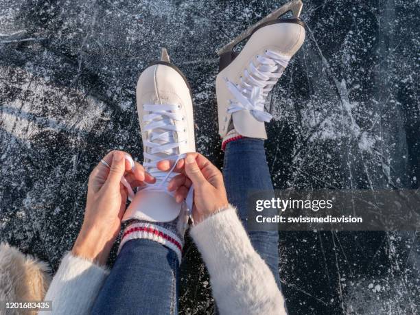 joven en el lago congelado poniendo patines de hielo al atardecer preparándose para divertirse y disfrutar de las vacaciones de invierno - patinar fotografías e imágenes de stock