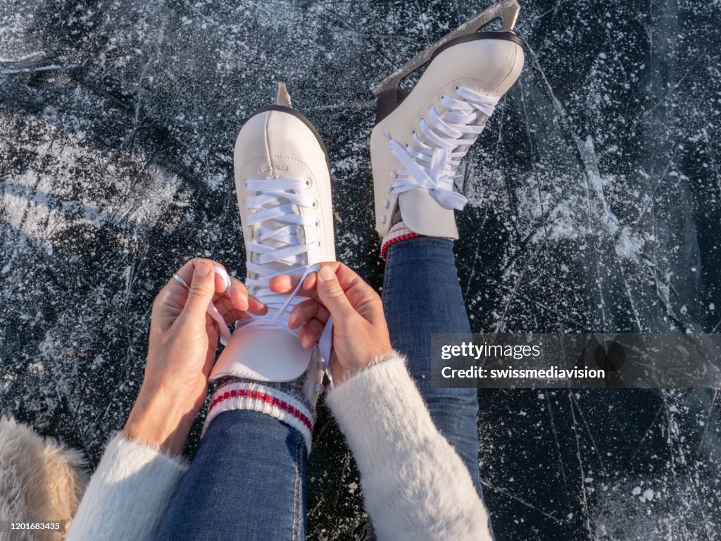 Young woman on frozen lake putting on ice skates at sunset getting ready to have fun and enjoy winter vacations