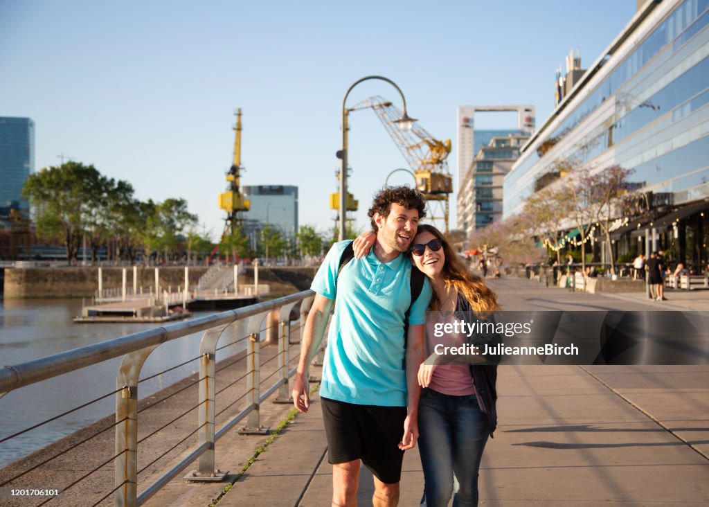 Couple closely walking together along dockside casually looking at modern buildings of Puerto Madero