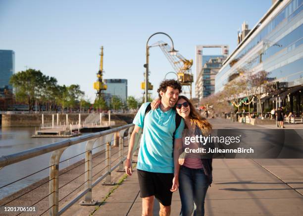 couple closely walking together along dockside casually looking at modern buildings of puerto madero - buenos aires port stock pictures, royalty-free photos & images