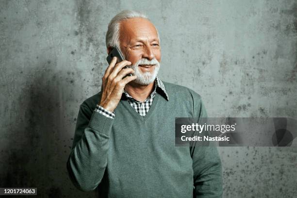 homem sênior de suéter segurando telefone inteligente falando - smart casual - fotografias e filmes do acervo