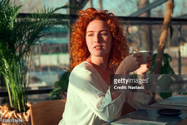 redhead woman with a cup of coffee on the cafe veranda - coffee on patio stock pictures, royalty-free photos & images