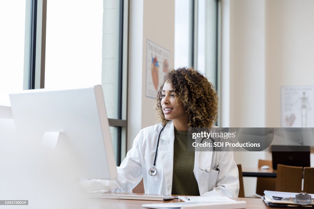 Medico femmina adulto medio esamina i record dei pazienti sul PC desktop