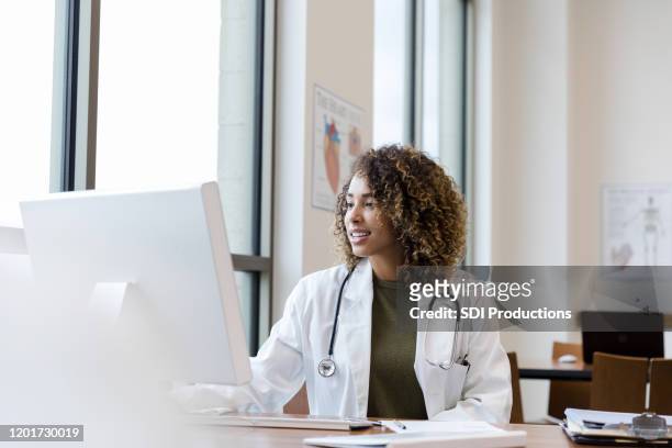 mid adult female doctor reviews patient records on desktop pc - using computer stock pictures, royalty-free photos & images