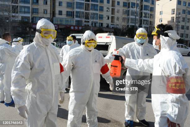 This photo taken on February 18, 2020 shows members of a police sanitation team having their protective suits disinfected after they sprayed...