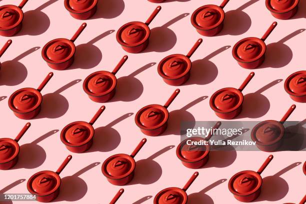 repeated old red kitchen pan on pink background - pots and pans stock-fotos und bilder