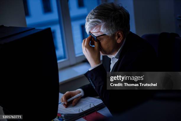 Photo posed: symbolic image on the subject of workload. A man sits exhausted at a desk late in the evening on February 18, 2020 in Berlin, Germany.