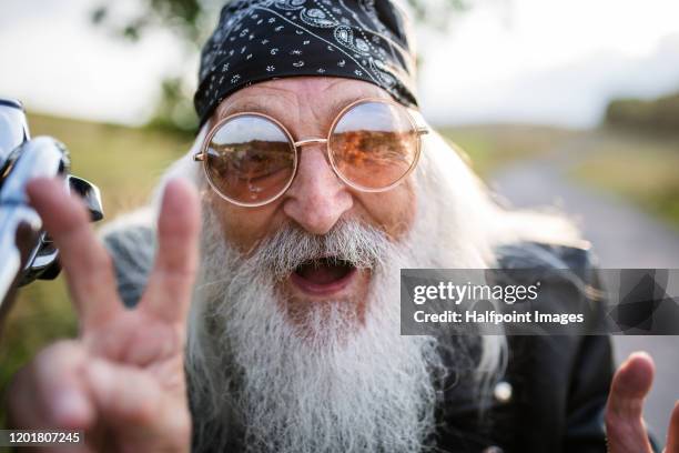 portrait of senior man rider with motorbike in the countryside, having fun. - old hipster stock-fotos und bilder