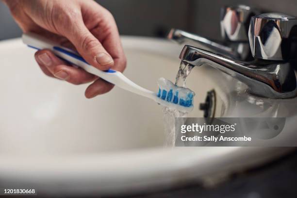 woman running toothbrush under a tap - toothbrush imagens e fotografias de stock