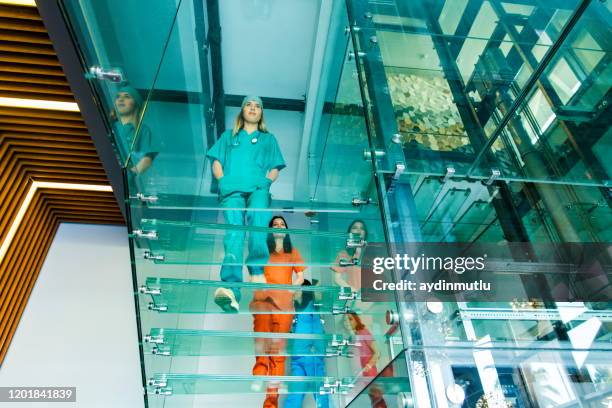 medical professionals walking on modern glass staircases - colorful medical scrubs stock pictures, royalty-free photos & images