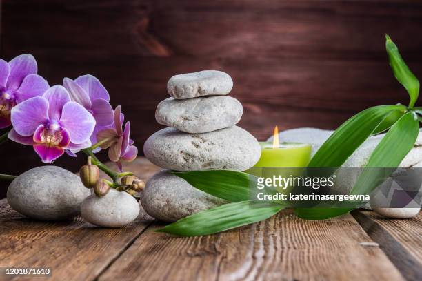 白い禅のバランスの石、蘭の花、竹の植物と木のテーブルの上のろうそく - 石庭 ストックフォトと画像
