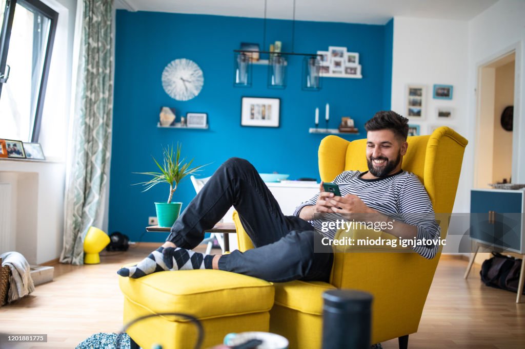 Glücklich bärtigen Mann sitzt auf Sessel und mit Smartphone