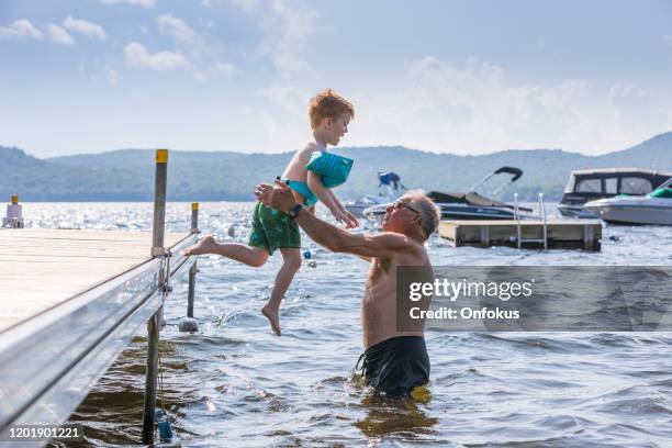 little redhead boy jumping in the lake with his grandfather in summer - old people diving stock pictures, royalty-free photos & images