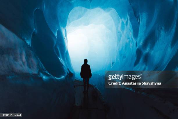 woman exploring the world of a big glacier inside the ice cave in switzerland - cave stock pictures, royalty-free photos & images
