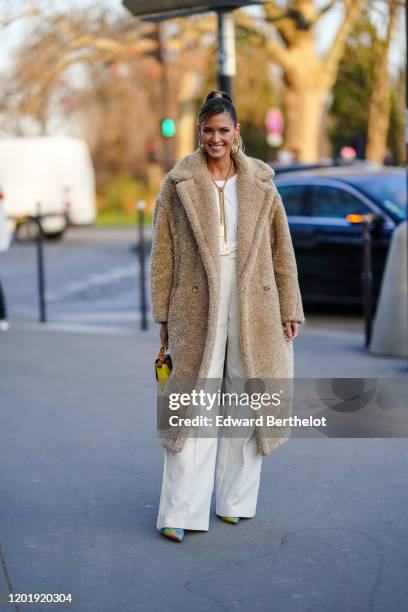 Helena Bordon wears earrings, a Chanel necklace, a glittering beige fluffy coat, a white top, white wide-legs full-length pants, a yellow and brown...