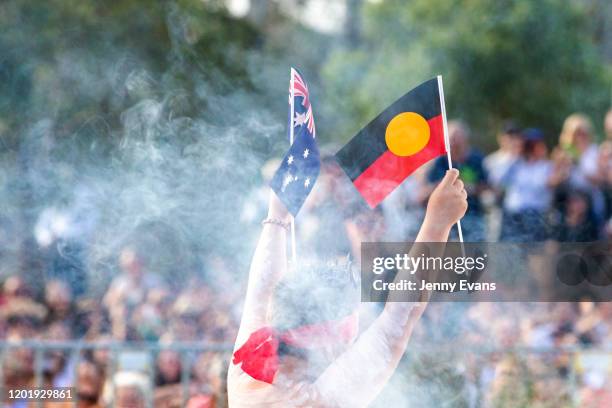 Member of the Koomurri dancers holds up an Indigenous and Australian flag during the WugulOra Morning Ceremony on Australia Day at Walumil Lawns,...