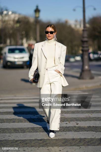 Pernille Teisbaek wears sunglasses, earrings, a white turtleneck pullover, an oversized blazer jacket, a Chanel quilted bag, flare pants, pointy...
