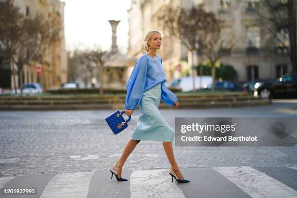 Leonie Hanne wears a blue silky lustous blouse with puff sleeves, a blue quilted Lady Dior bag, a pale blue leather skirt, Dior pointy shoes, during...