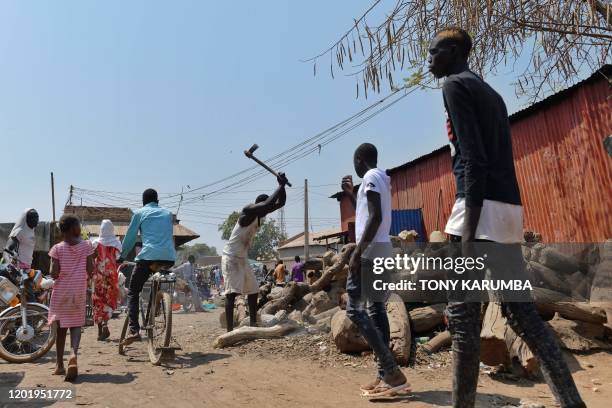 Man hacks at logs with an axe as people walk past at an open market in Wau on February 2, 2020. - 13,000 civilians shelter under UN protection at the...