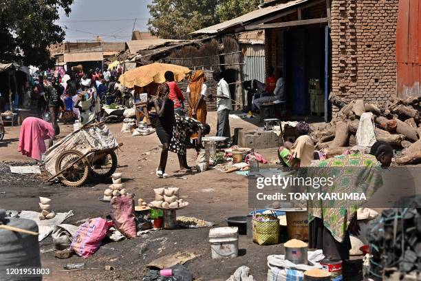 Man hacks at logs with an axe as people walk past at an open market in Wau on February 2, 2020. - 13,000 civilians shelter under UN protection at the...