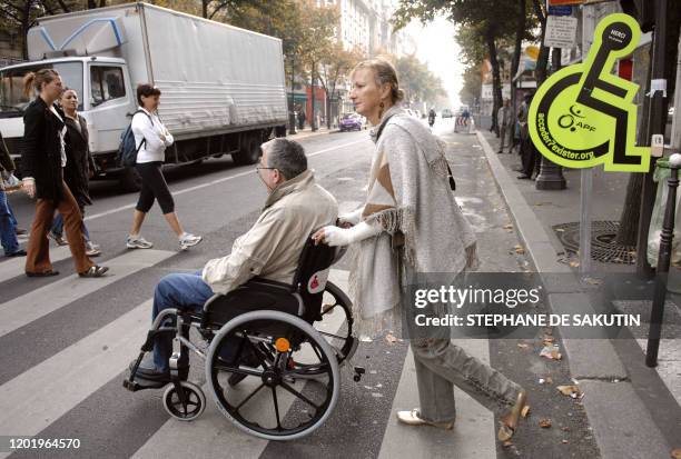 Une personne poussant un handicapé en fauteuil roulant, le 08 octobre 2007 à Paris, traverse un passage piéton devant une silhouette verte marquée du...