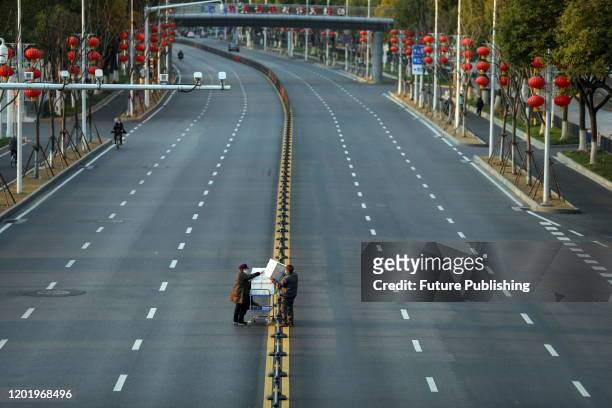 Two workers try to get boxes of vegetables over the barriers in the empty road outside the Union Hospital in Wuhan in central China's Hubei province...
