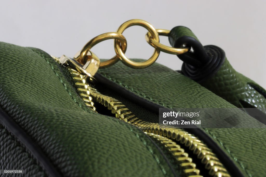 Green handbag with unzipped gold colored zipper with three metal rings attached