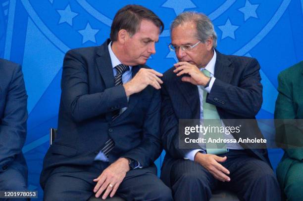 President of Brazil Jair Bolsonaro talks with Brazil's Economy Minister Paulo Guedes during the "Ceremony of the New Housing Credit Program" at the...