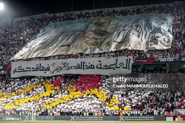 Zamalek SC's fans wave a giant banner showing an Egyptian pharaoh standing before white-coloured ancient city walls, with another beneath reading in...