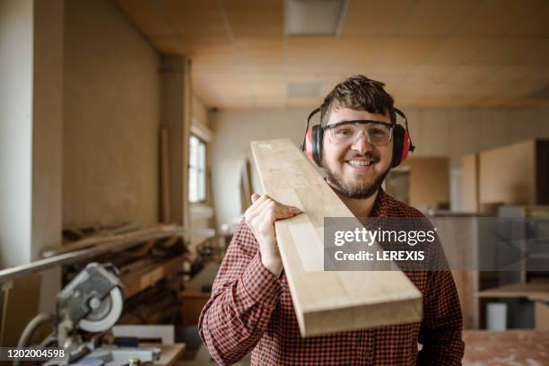 a smiling carpenter carries a beam of work - carpenter imagens e fotografias de stock