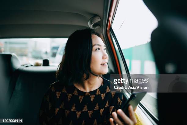 asiatische frau sitzt im hinteren teil eines taxis und schaut aus dem fenster und lächelt beim pendeln in der stadt - back of car stock-fotos und bilder