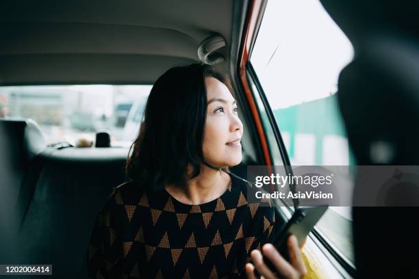 asian woman sitting in the back of a taxi looking out the window and smiling while commuting in the city - tourist china stock pictures, royalty-free photos & images