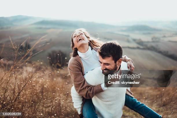 cheerful couple having fun while piggybacking in autumn day outdoors. - happiness imagens e fotografias de stock